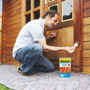 Mann streicht Holz mit Xyladecor Holzschutz-Lasur Palisander. 2in1 Holzlasur für Aussen.