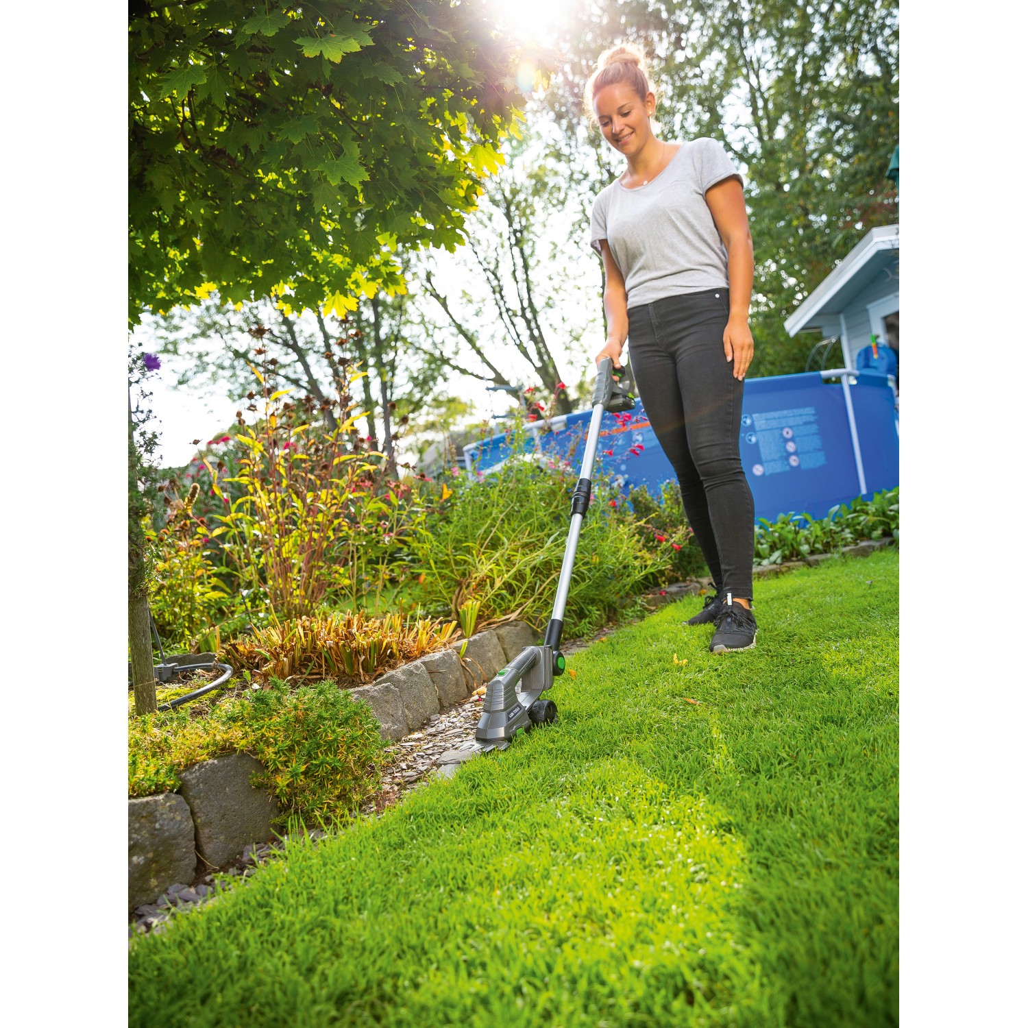 Frau nutzt LUX Akku-Grasscheren-Set mit Teleskopstiel im Garten für präzise Rasenkanten.