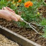 Kent & Stowe Handgrubber mit 3 Zinken im Einsatz im Gartenbeet. Gartenhandgerät mit Holzgriff.