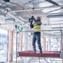 Handwerker bohrt mit Bosch Akku-Bohrhammer GBH 18V-22 im Combi-Kit an Decke, stehend auf Gerüst.