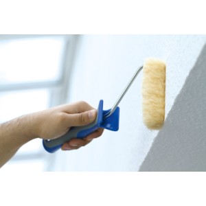 Hand hält LUX Lammfellwalze (25 cm) beim Streichen einer Wand. Farbwalze mit blauem Griff.