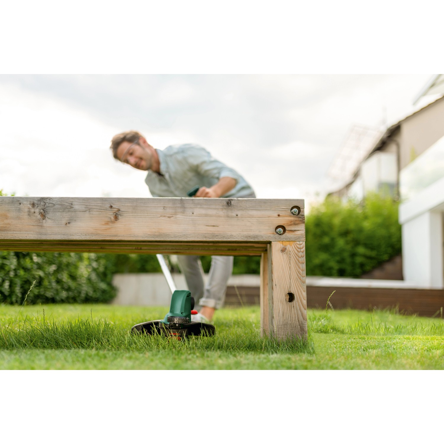 Bosch Akku-Rasentrimmer UniversalGrassCut 18V-26 im Einsatz unter einer Holzkonstruktion.