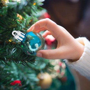 Kinderhand hängt glänzende petrolfarbene Weihnachtskugel an Tannenbaum. Festliche Christbaumdeko.
