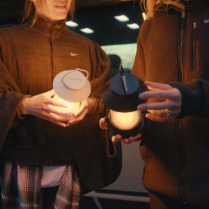 Zwei Personen halten Horntools Campinglampen (schwarz/weiß) mit warmem Licht.