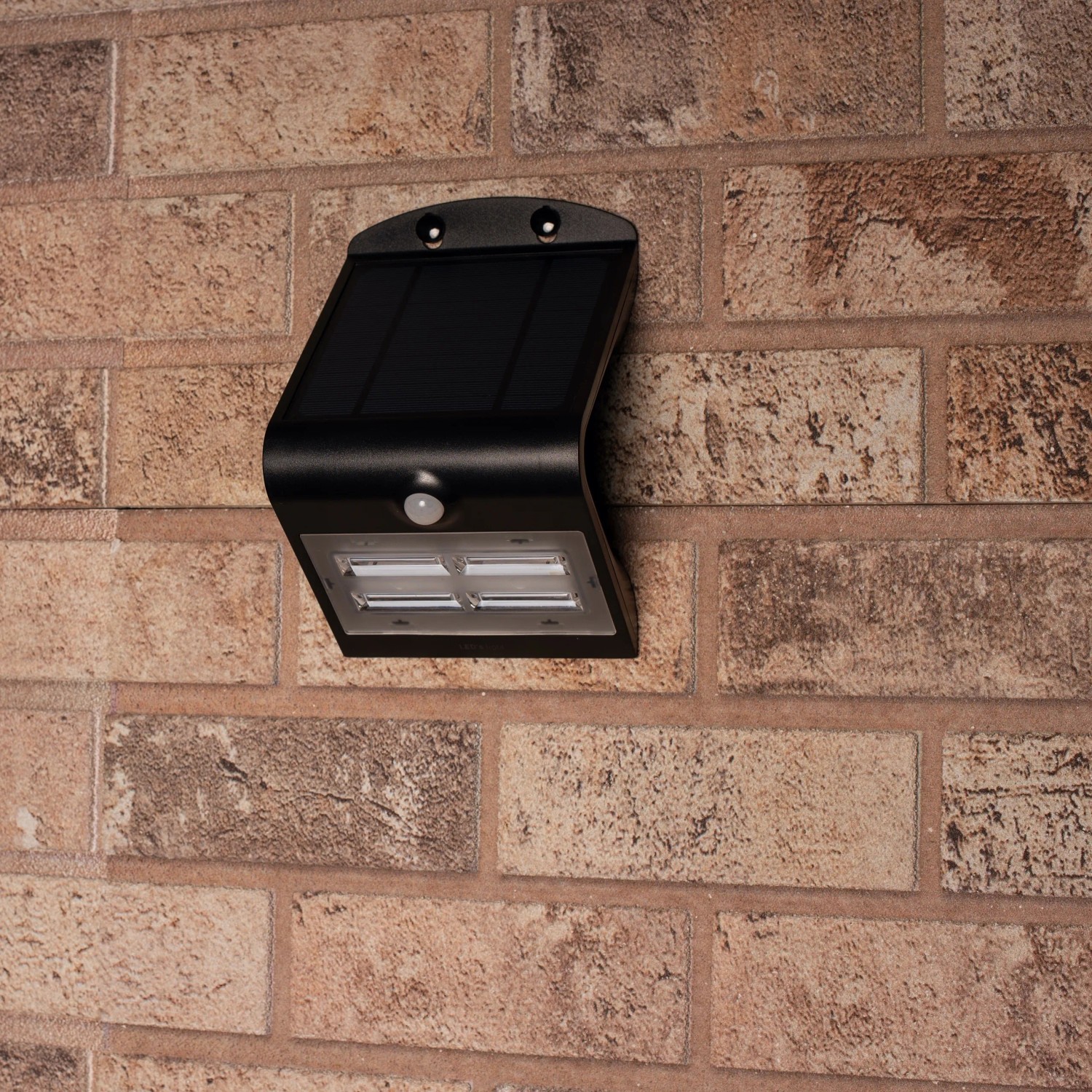 Schwarze LED Solar-Außenleuchte mit Sensor an einer Backsteinwand.