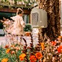 Elho Insektenhotel Cosy, beige-weiß, an Baum befestigt, mit Kind und Blumen im Garten.