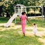 Axi Beach Tower Spielturm mit Doppelschaukel und weißer Rutsche im Garten mit Mutter und Kind.