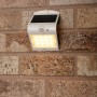 Weiße LED Solar-Außenleuchte mit Sensor an einer Backsteinwand. Flutlicht mit 220 Lumen.