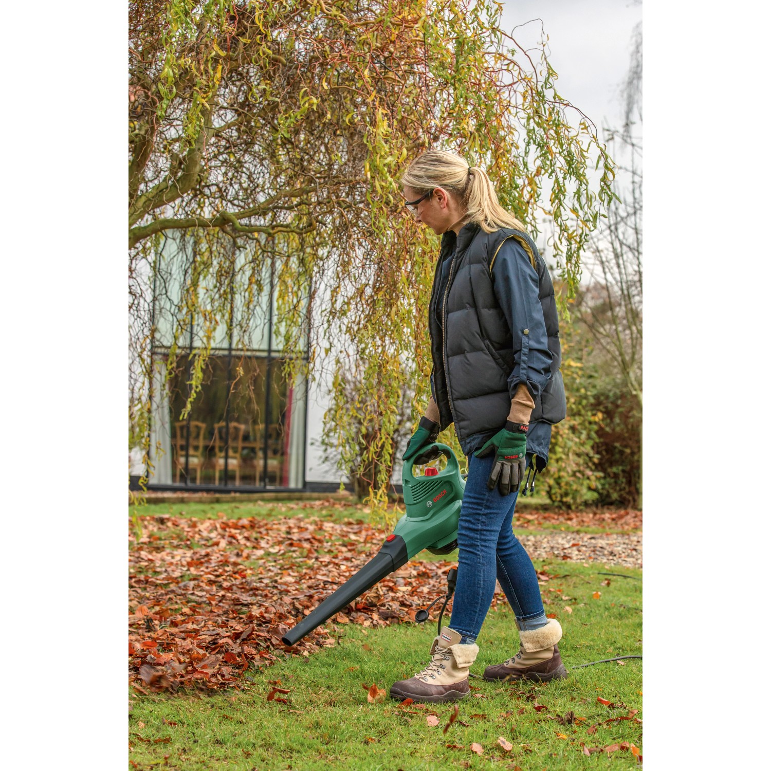 Frau nutzt Bosch UniversalGarden Tidy 2300 Gartensauger zum Laubsaugen.