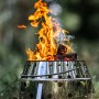 Petromax Atago Grill-Set: Graue Feuerschale mit Feuer und Grillspießen im Outdoor-Einsatz.
