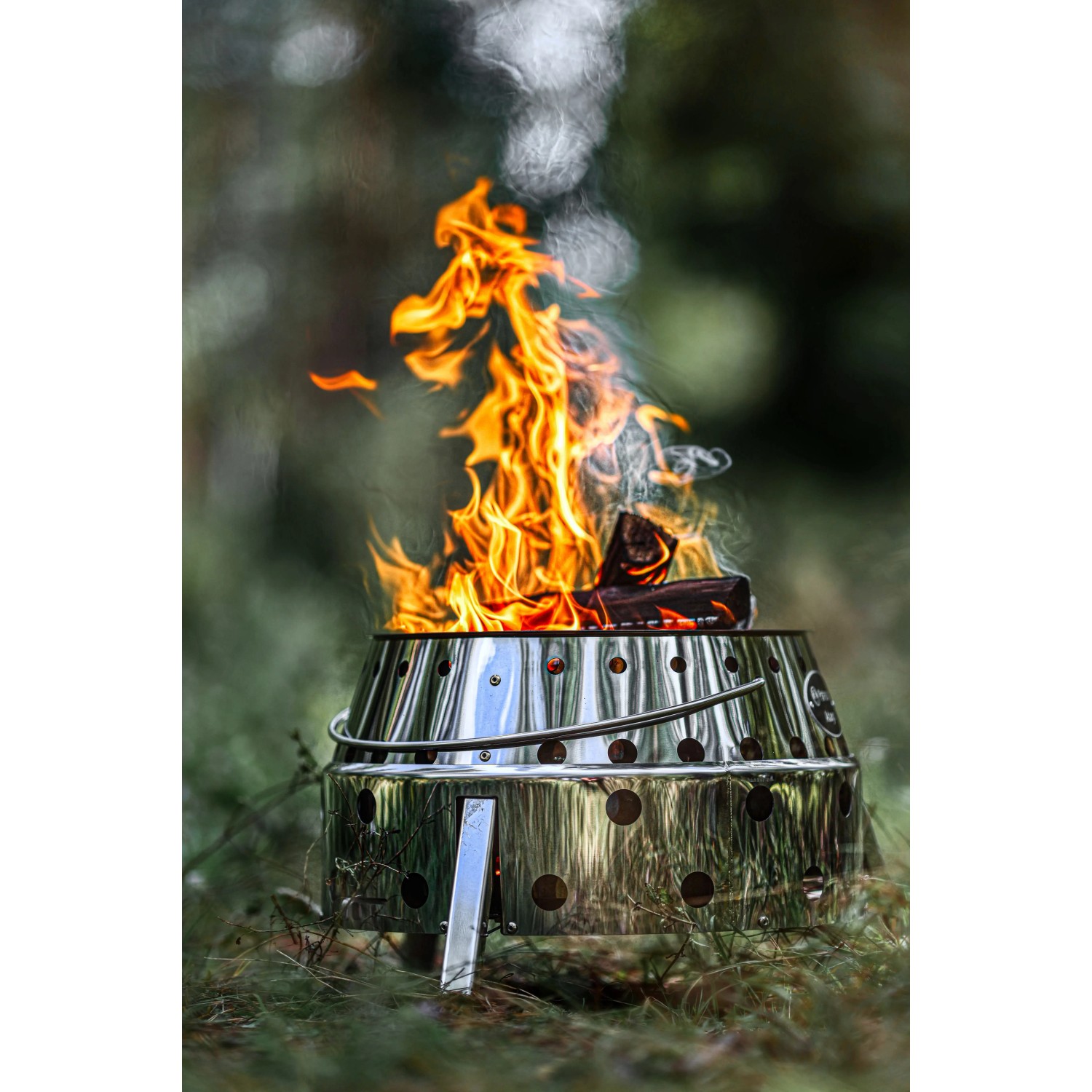 Petromax Atago Grill-Set: Graue Feuerschale mit Feuer und Grillspießen im Outdoor-Einsatz.