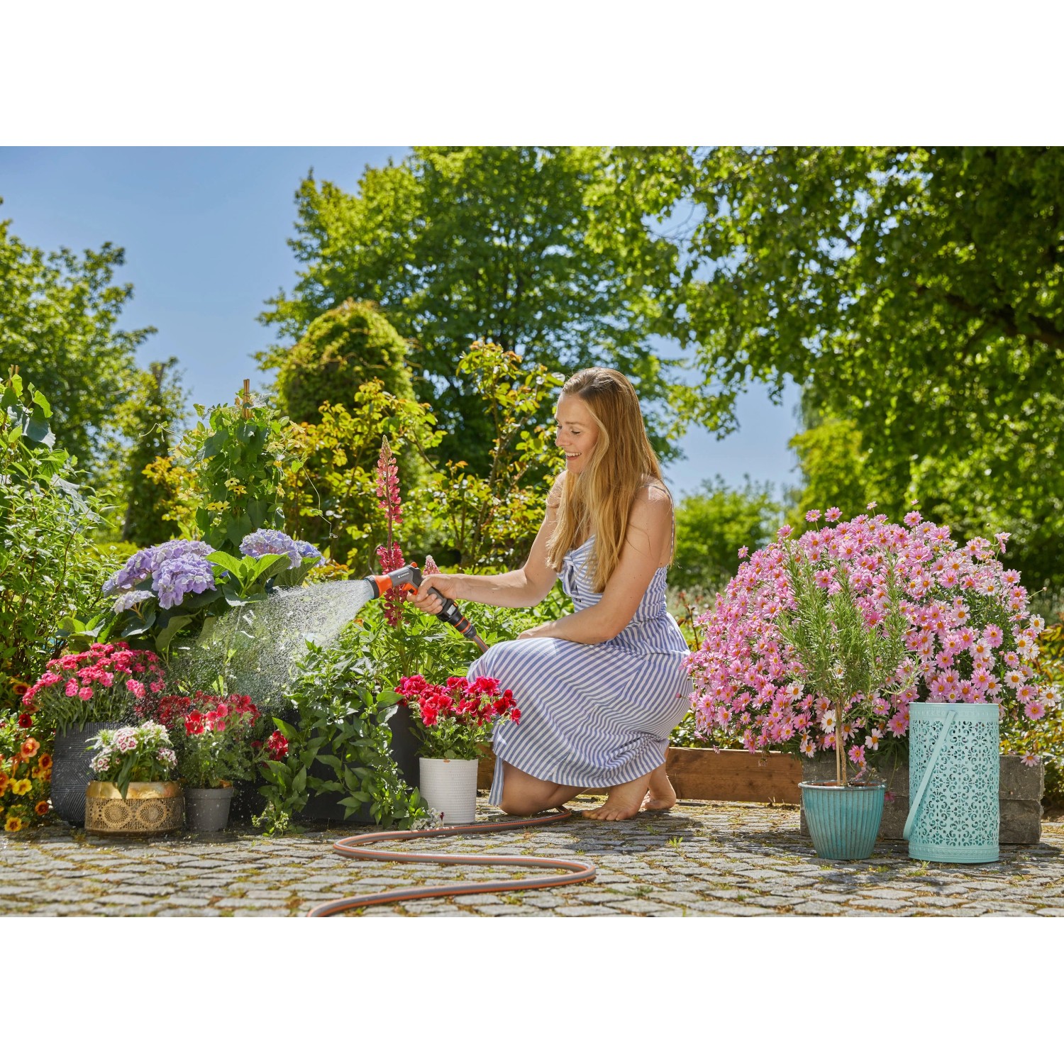 Frau bewässert Blumen mit Gardena Bewässerungsbrause AquaCount im Garten.