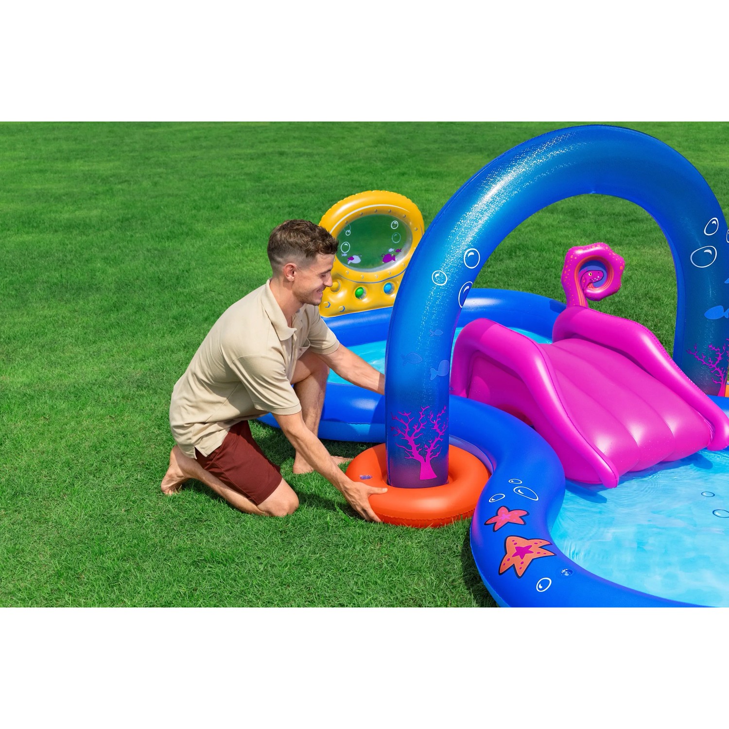 Bestway Wasserspielcenter Unterwasserwelt (330x188x117cm) mit Rutsche, Sprinkler und Mann beim Aufbau.