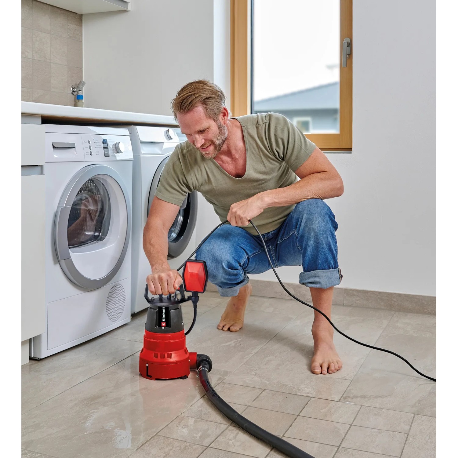 Mann bedient rote Einhell GC-DP 6935 LL Schmutzwasserpumpe im Keller neben Waschmaschinen.