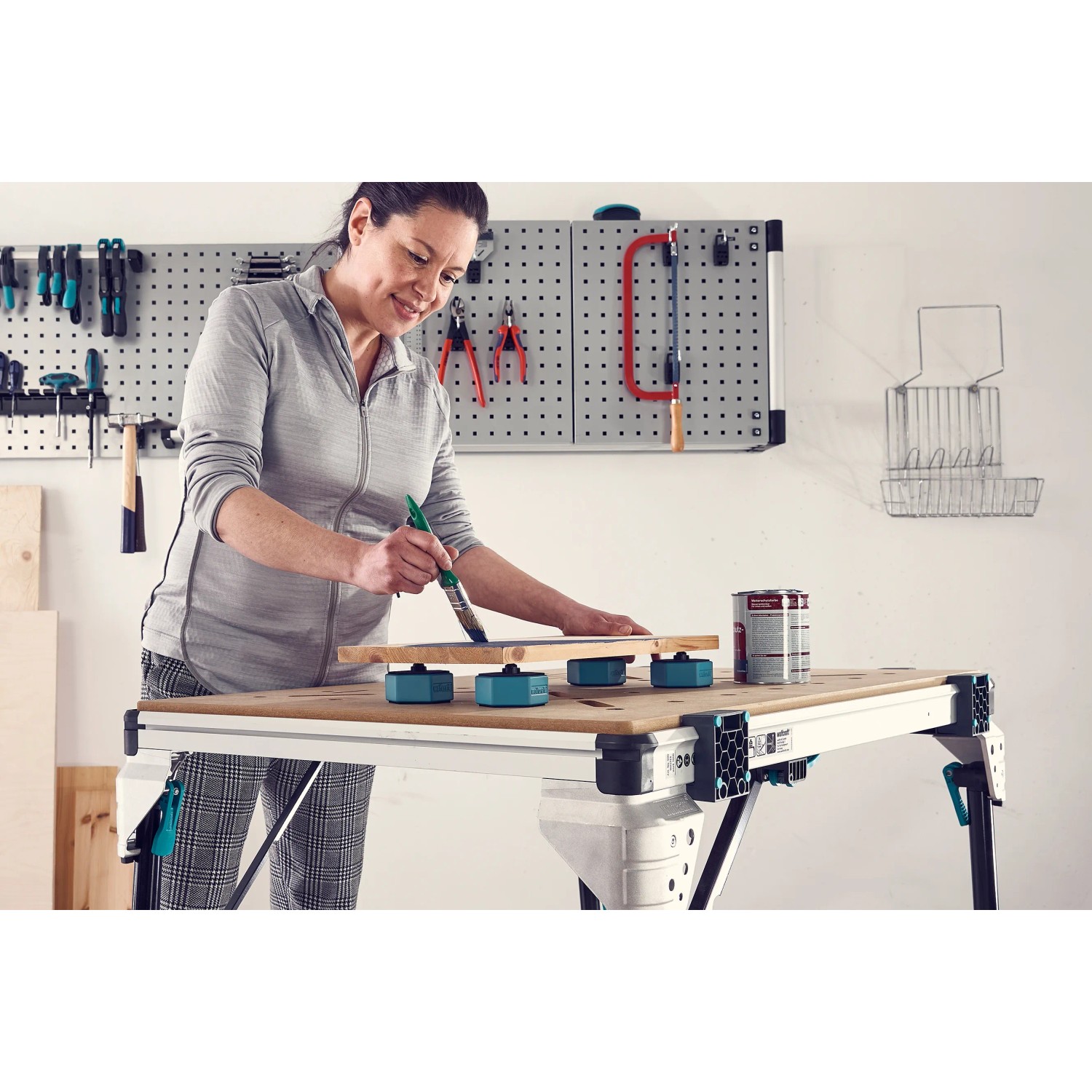 Frau lackiert Holz auf Werkbank mit wolfcraft Werkstückauflagen-Set.