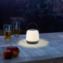 Schwarz-weiße LED-Akku-Tischleuchte Cecina (Ø 14 cm) auf Holztisch im Außenbereich.