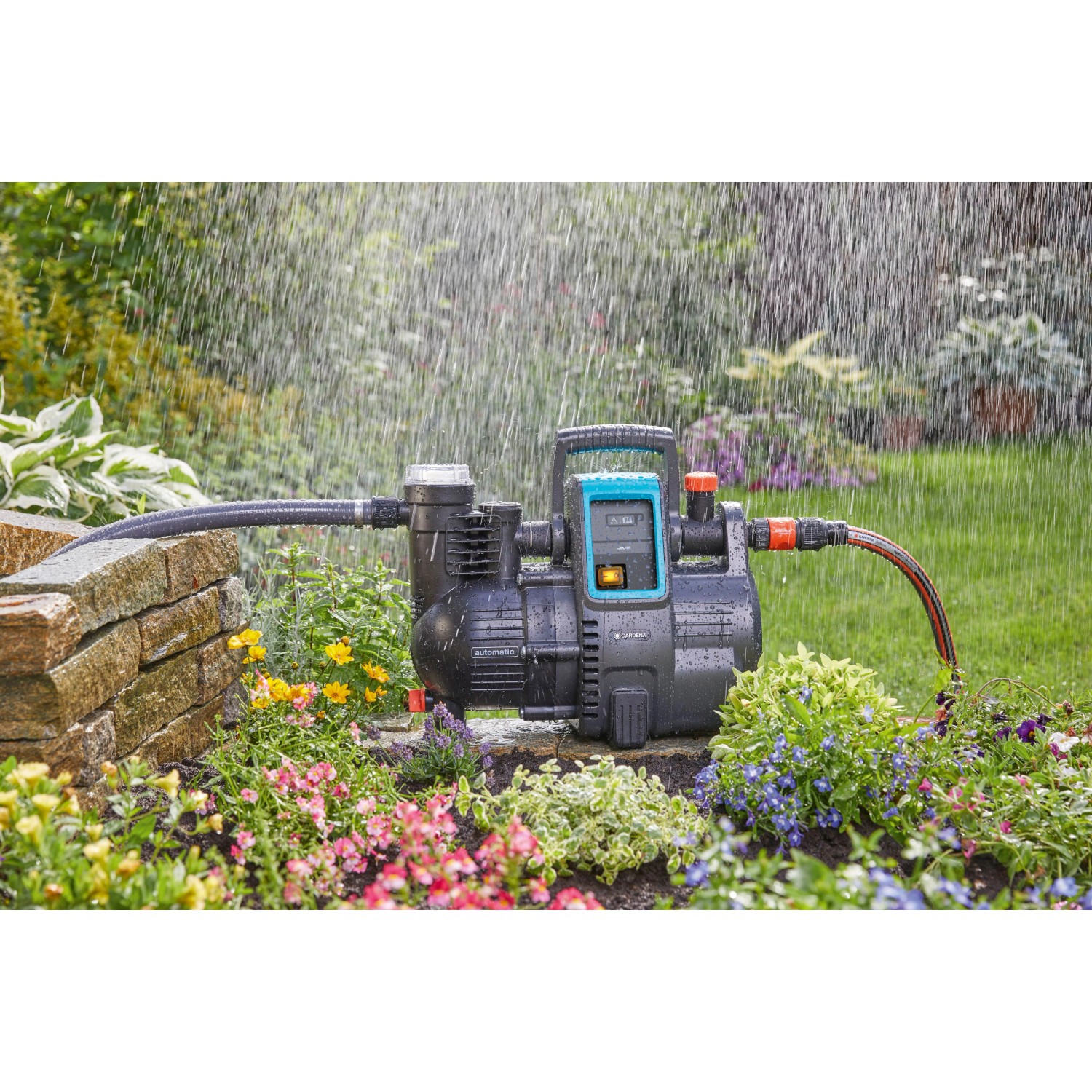 Gardena Haus- und Gartenautomat 4000/5 im Einsatz: Graue Gartenpumpe mit blauem Display bewässert Blumen.