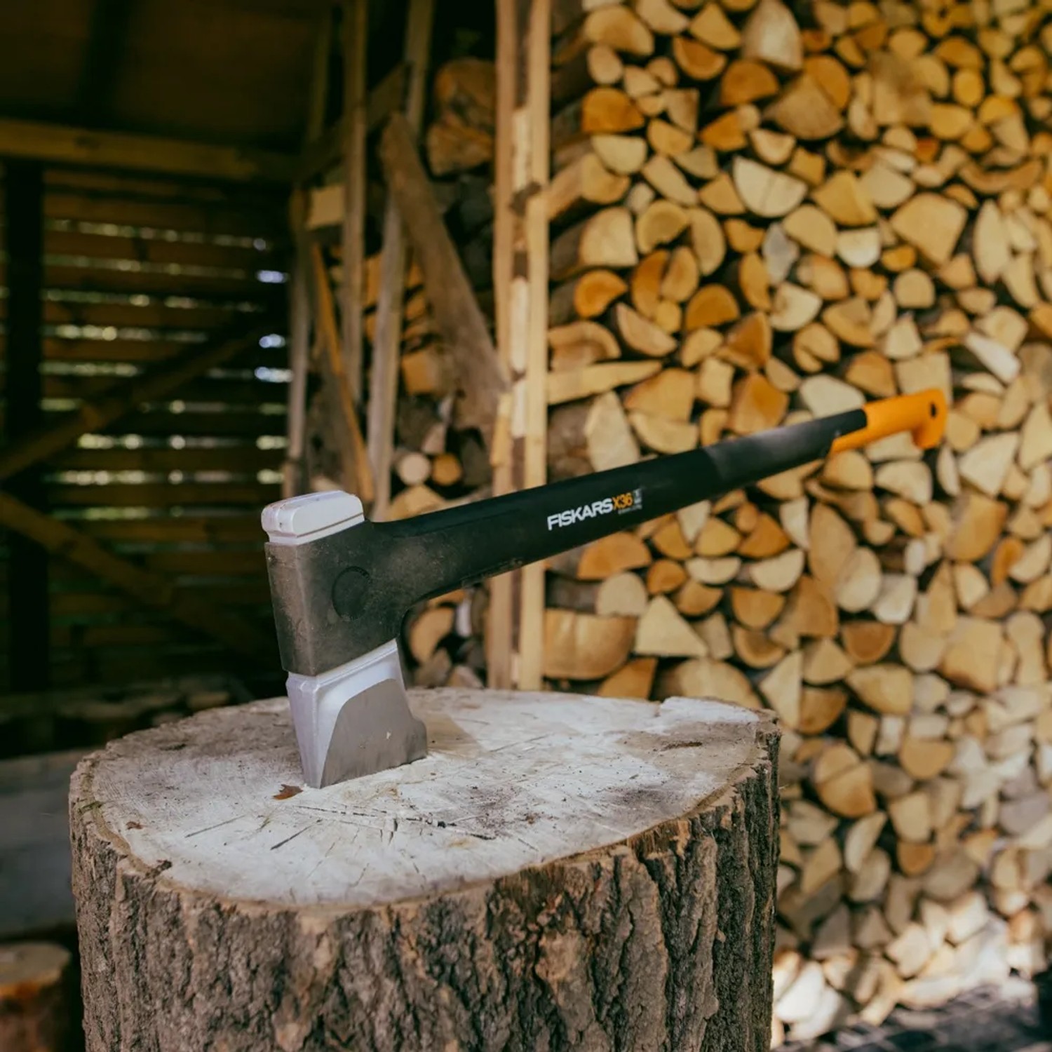 Fiskars X-series Spalt-Axt X36 (91,5 cm) auf Holzscheit vor Holzstapel.