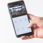 Hand hält Smartphone mit App der Summer Fun Smart Garden Cam. Kameraüberwachung im Garten.