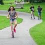 Mädchen fährt hellblauen Six Degrees Aluminium Scooter auf einem Weg im Park.