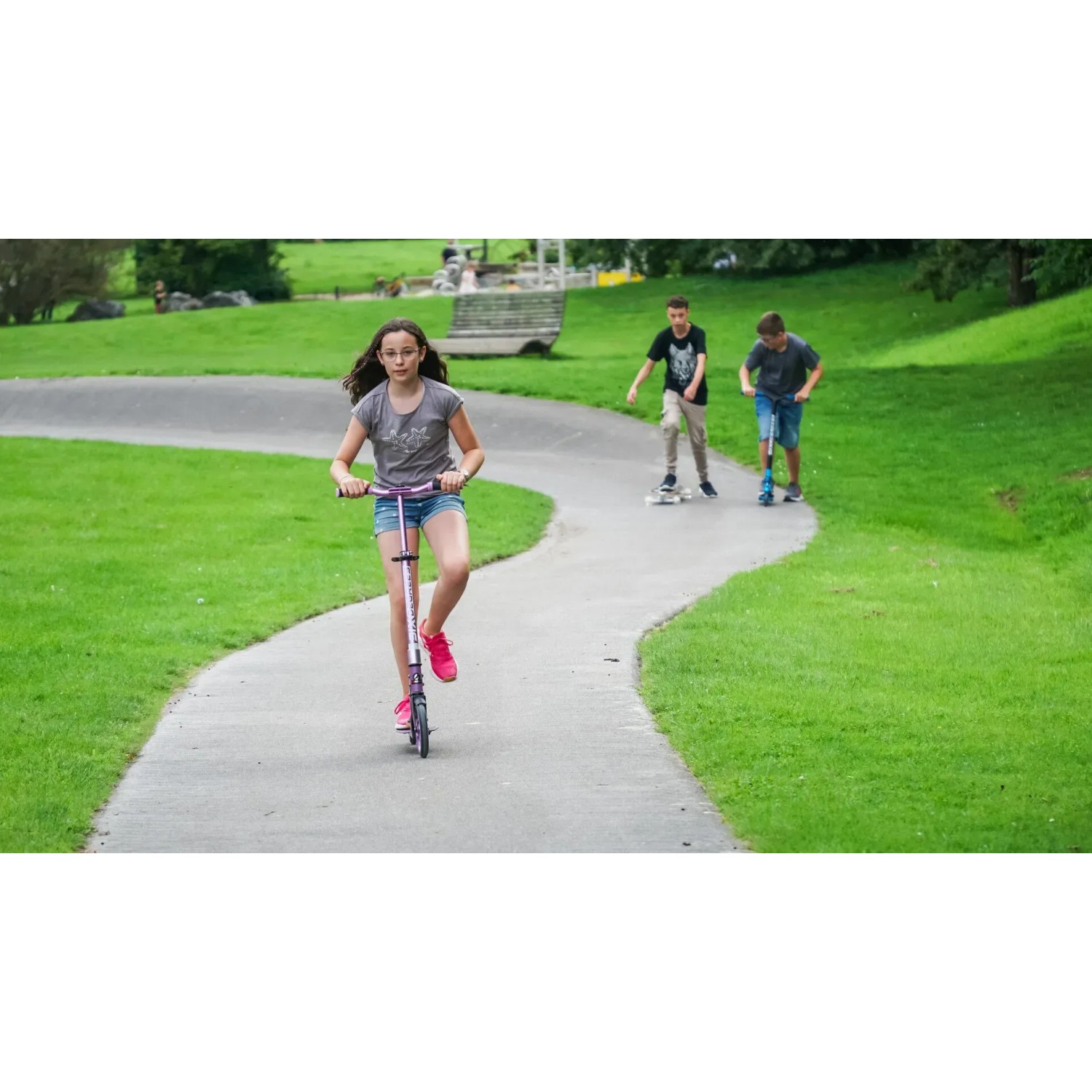 Mädchen fährt hellblauen Six Degrees Aluminium Scooter auf einem Weg im Park.