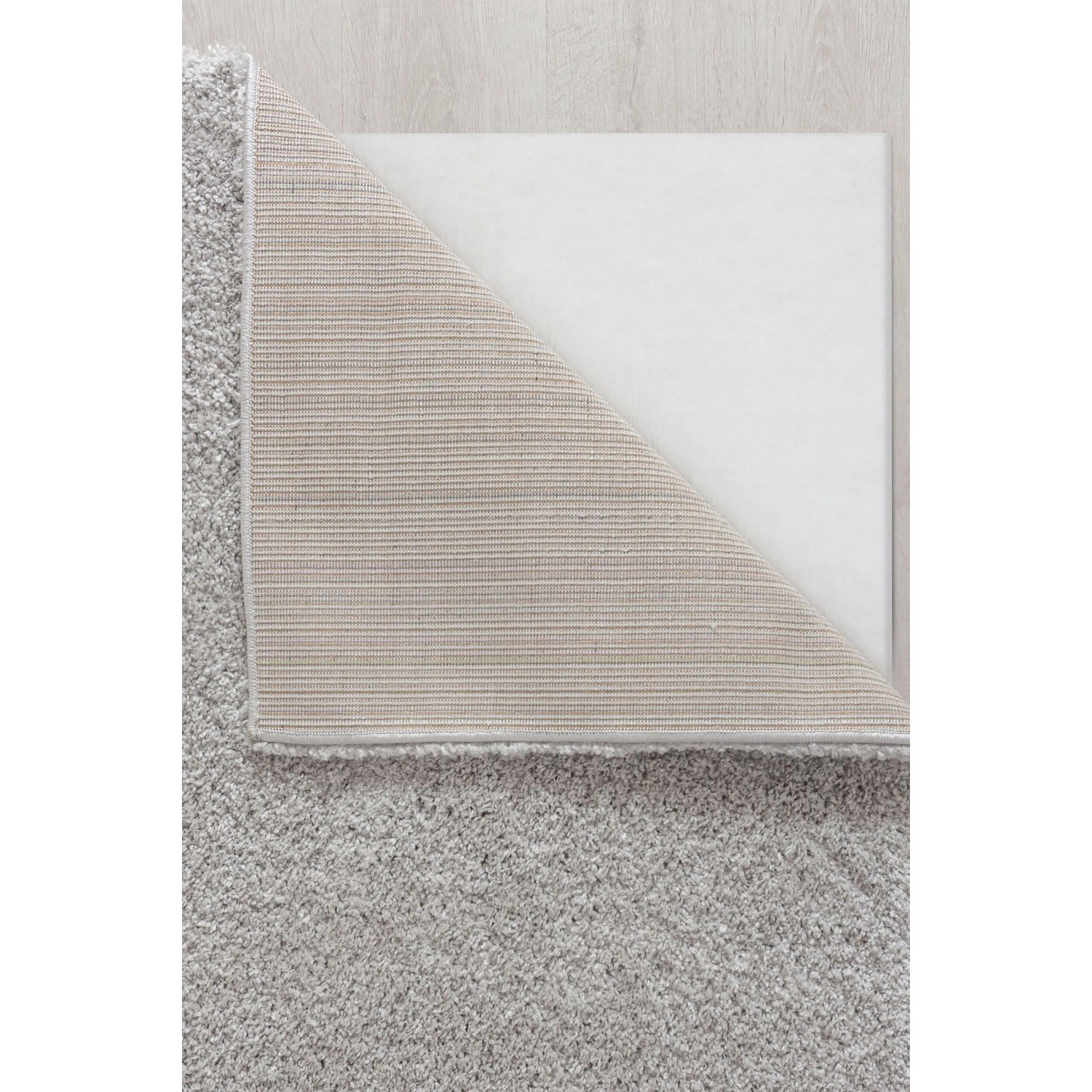Grauer Flair Rugs Hochflorteppich Feather Soft mit zotteligem Flor. Eine Ecke zeigt die Jute-Unterlage auf hellem Holzboden.