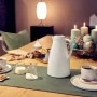 Weiße Isolierkanne Harmonic (1 l) auf gedecktem Tisch mit Geschirr und Adventskranz.