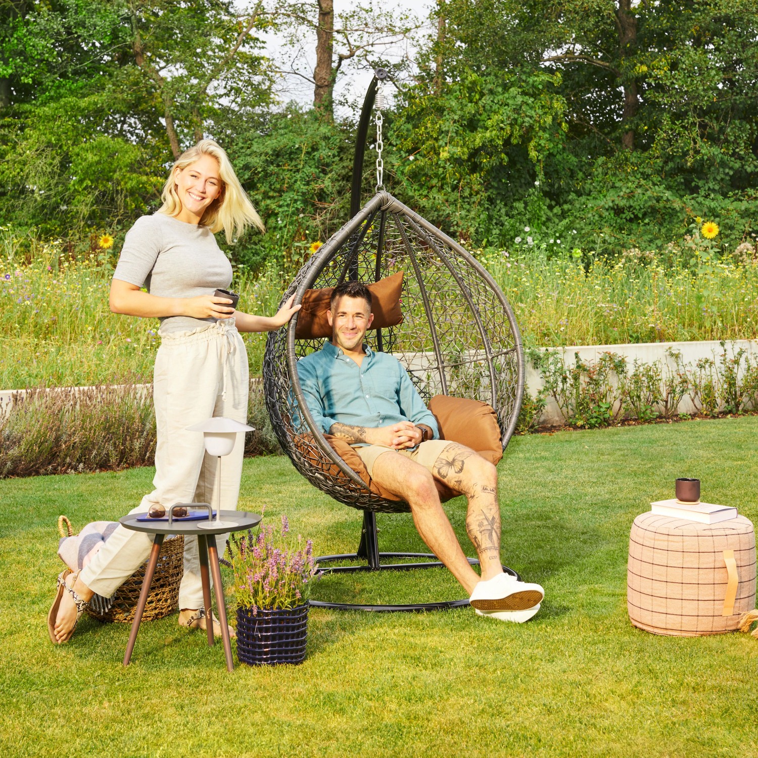 Grauer Home Deluxe Hängesessel Cielo Polyrattan mit Personen im Garten.