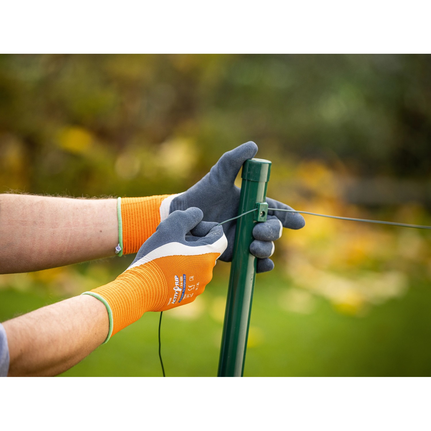 Hände mit LUX Arbeitshandschuhen Super Grip Gr. 9 befestigen Draht an einem Zaunpfahl.