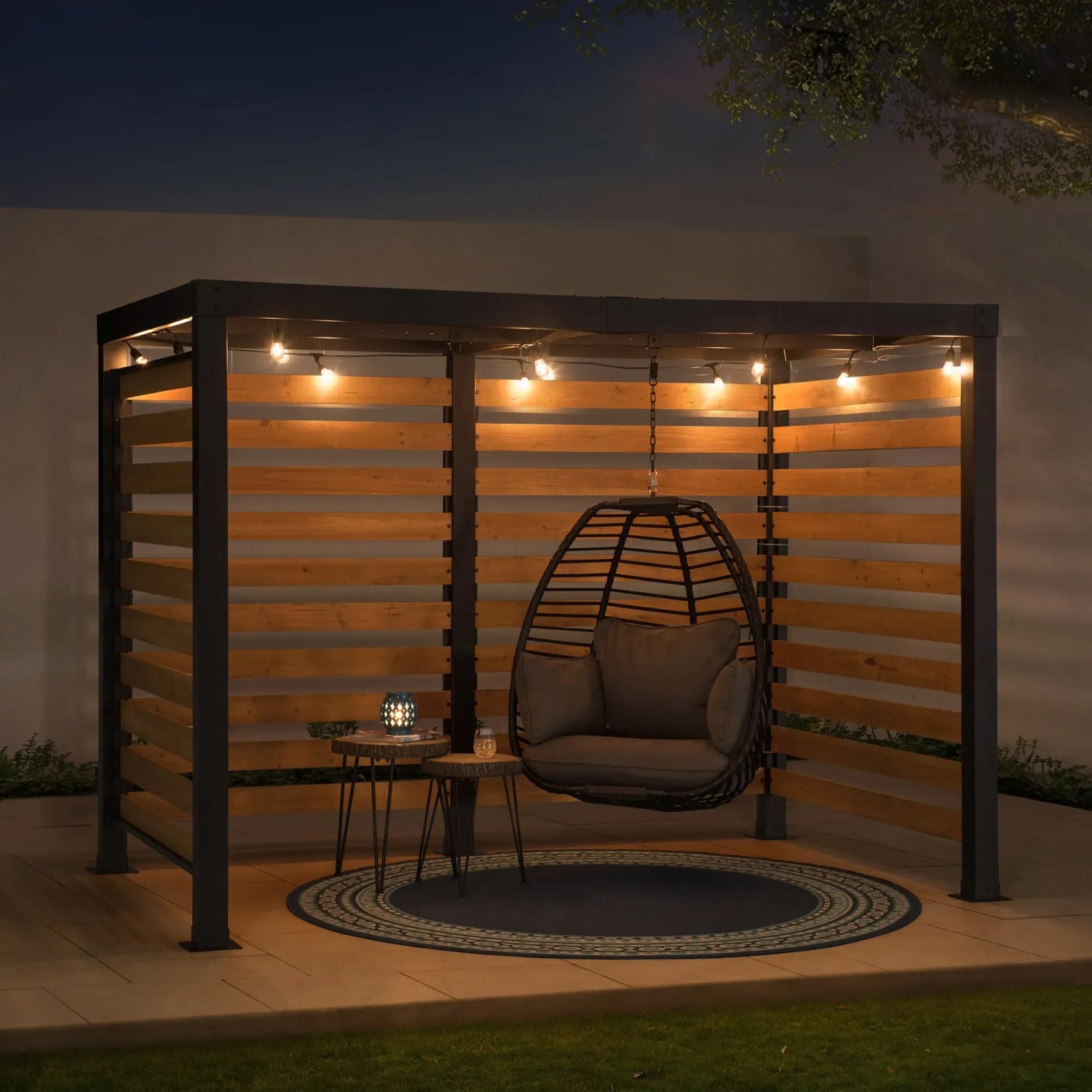 Schwarze Sunjoy Pergola Marao aus Stahl mit Zedernholz-Lamellen und Hängekorb mit Lichterkette.