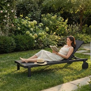 Schwarze DELUKE Sonnenliege RUNE mit Rollen im Garten, Frau entspannt lesend. Perfekt als Gartenliege oder Strandliege.