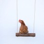 Braunes Huhn sitzt auf einer Hühnerschaukel mit Aufhängung vor weißer Wand.