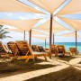Helle dreieckige Sonnensegel spenden Schatten über Liegestühlen am Strand. Ideal für Schwerlast Sonnensegel Befestigung.