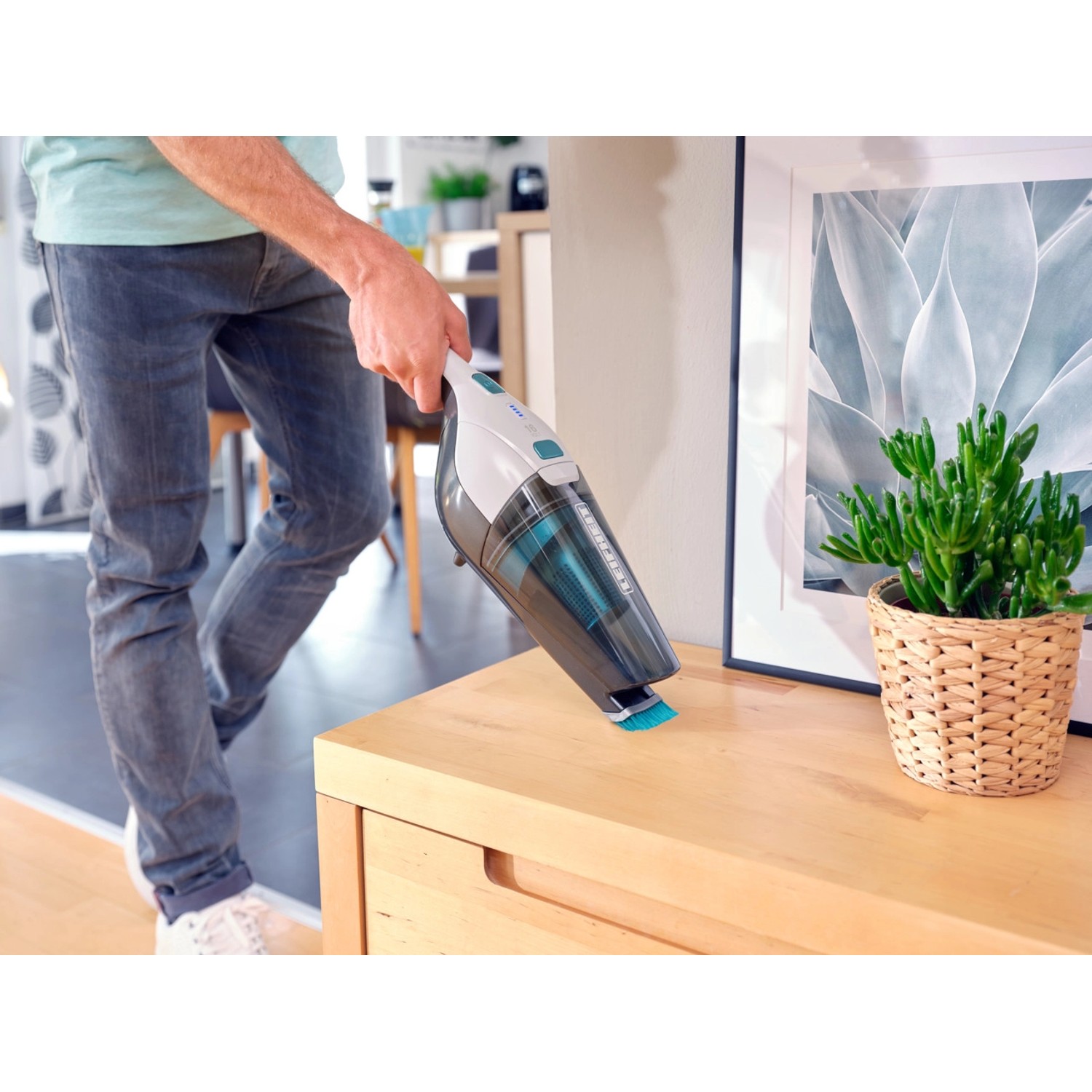 Mann saugt mit dem Leifheit Akku-Staubsauger Rotaro eine Kommode ab.