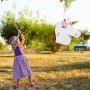 Kind schlägt weiße Einhorn Pinata mit bunter Mähne im Garten. Lustiges Partyspiel für Kindergeburtstage.