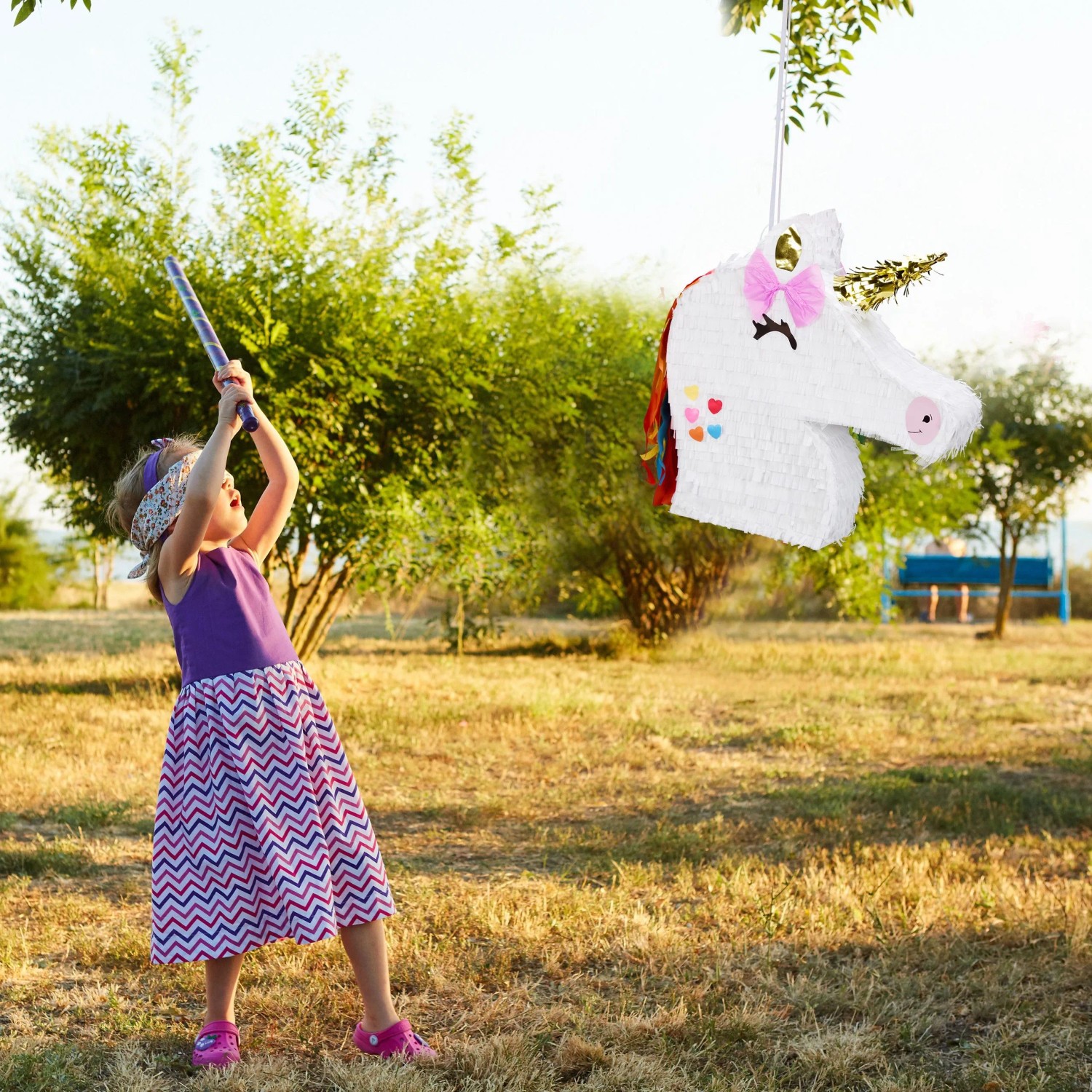 Kind schlägt weiße Einhorn Pinata mit bunter Mähne im Garten. Lustiges Partyspiel für Kindergeburtstage.