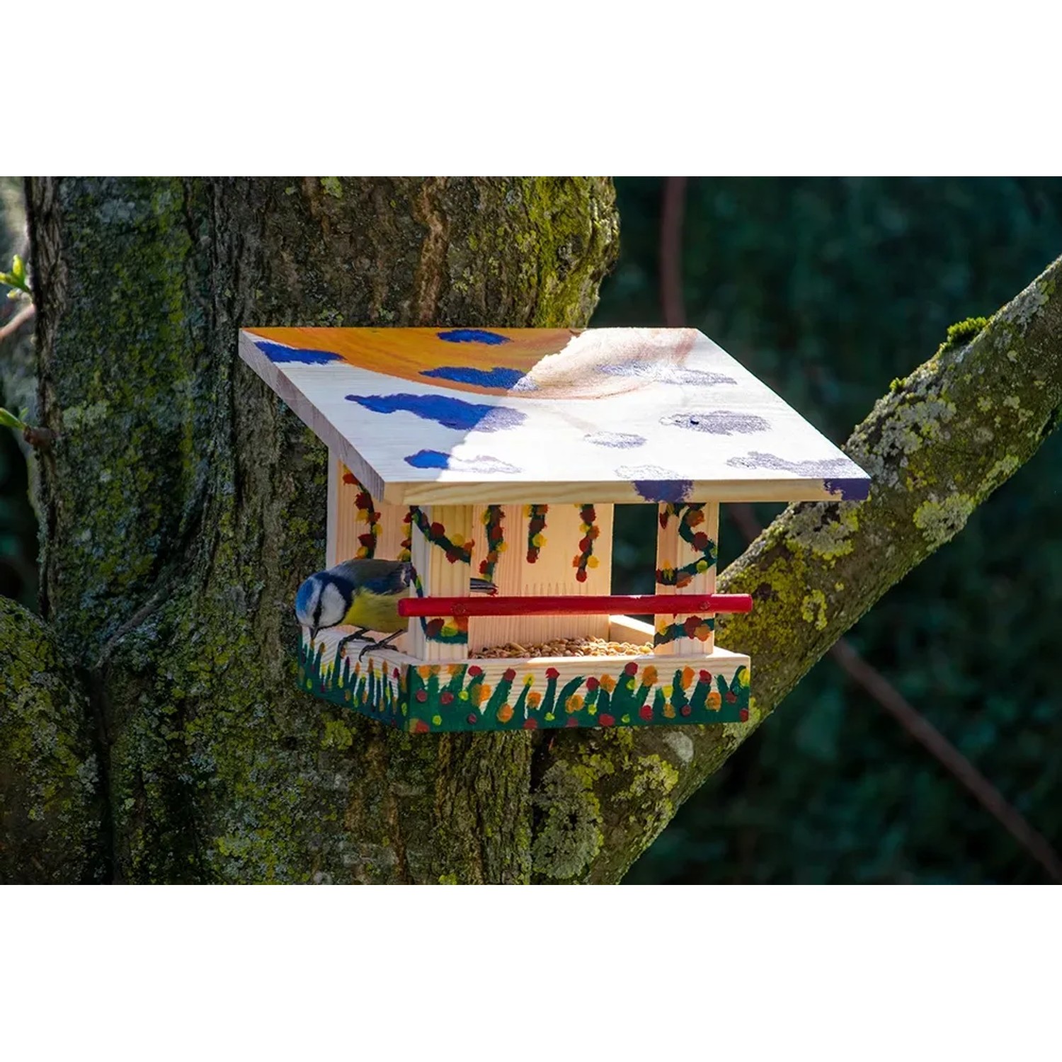 Bemaltes Dobar Vogelfutterhaus aus Kiefernholz mit Blaumeise an Baum.