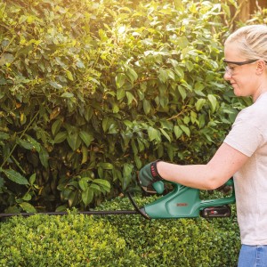 Frau schneidet Hecke mit Bosch Akku-Heckenschere EasyHedgeCut 18-45. Kabellose Heckenschere für präzise Schnitte.