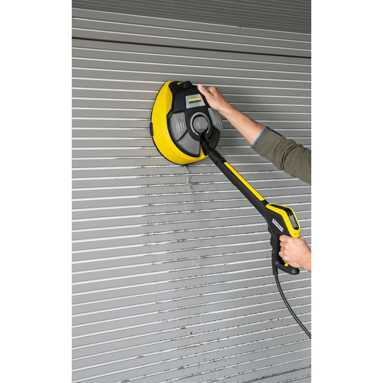 Kärcher Flächenreiniger T 7 Plus T-Racer im Einsatz an einer Garagenwand. Der gelbe Flächenreiniger wird mit der Hand geführt.
