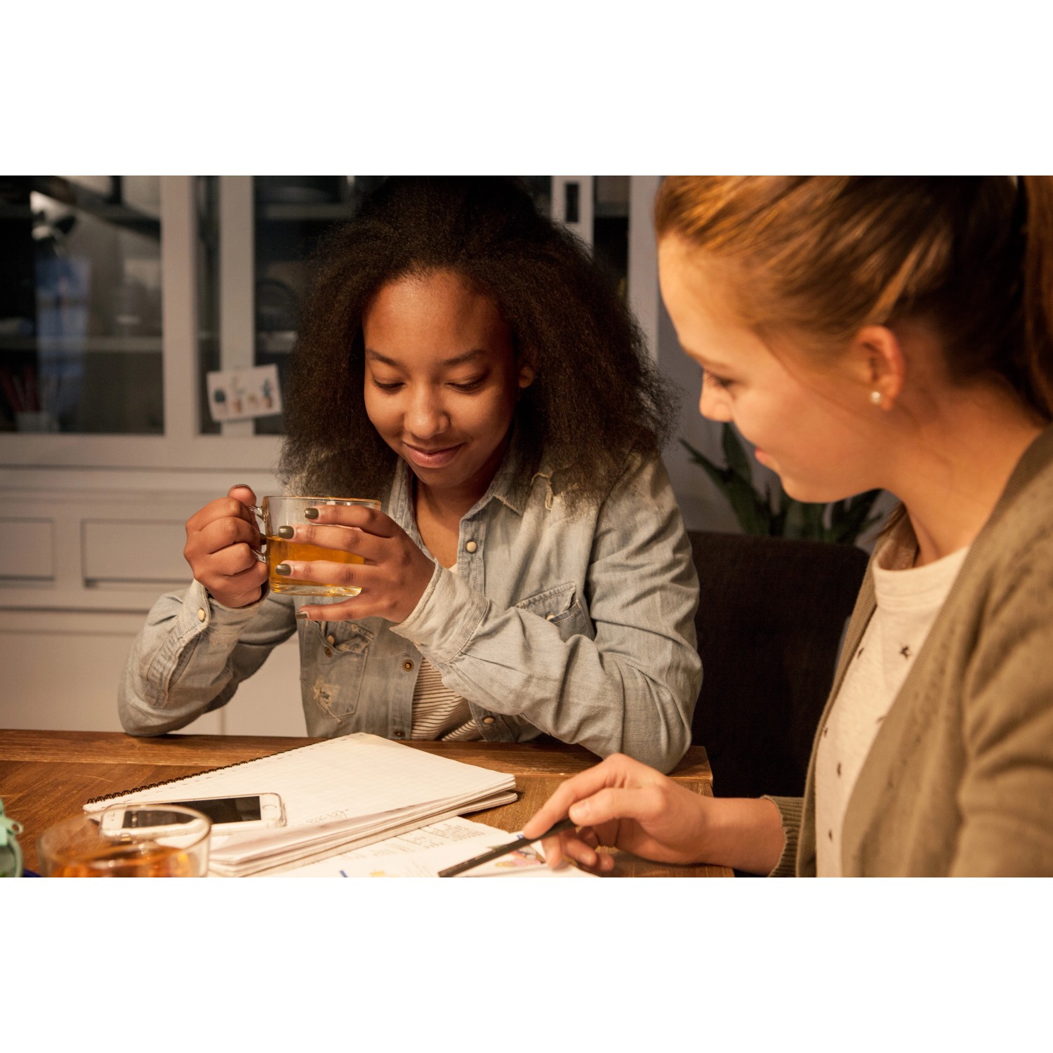 Szene mit zwei jungen Frauen an einem Tisch, beleuchtet durch ein Philips LED-Leuchtmittel E27, das warmes Licht spendet.