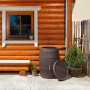 Garantia Regentonne Barrica 420L in Dunkelbraun vor Holzwand mit Fenster und Pflanzen.