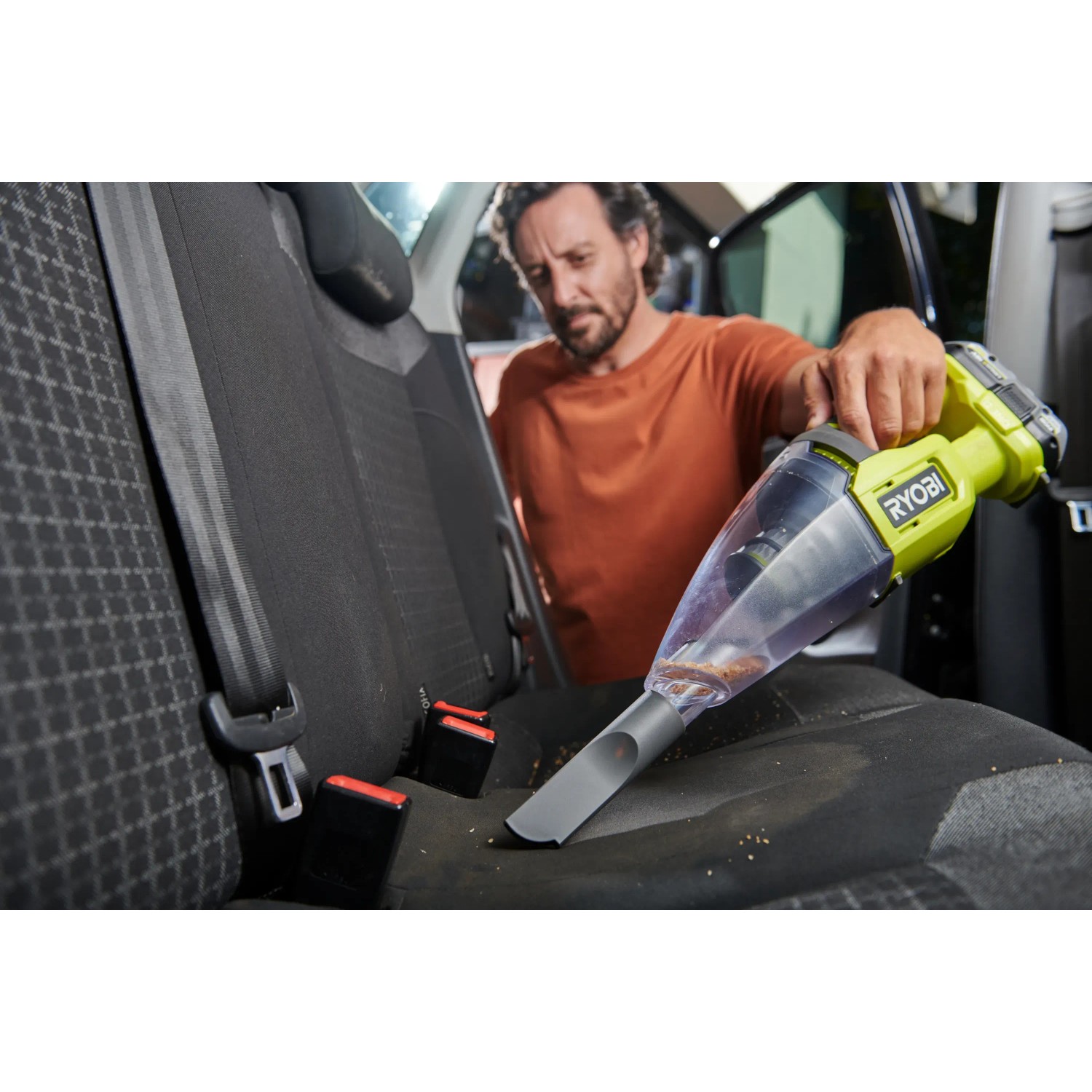 Mann saugt mit Ryobi Akku-Handsauger RHV18 einen Autositz. Der Handstaubsauger ist grün-grau.
