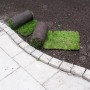 Rollrasen: Spiel- und Sportrasen als Rollen auf dunkler Erde neben Steinweg.