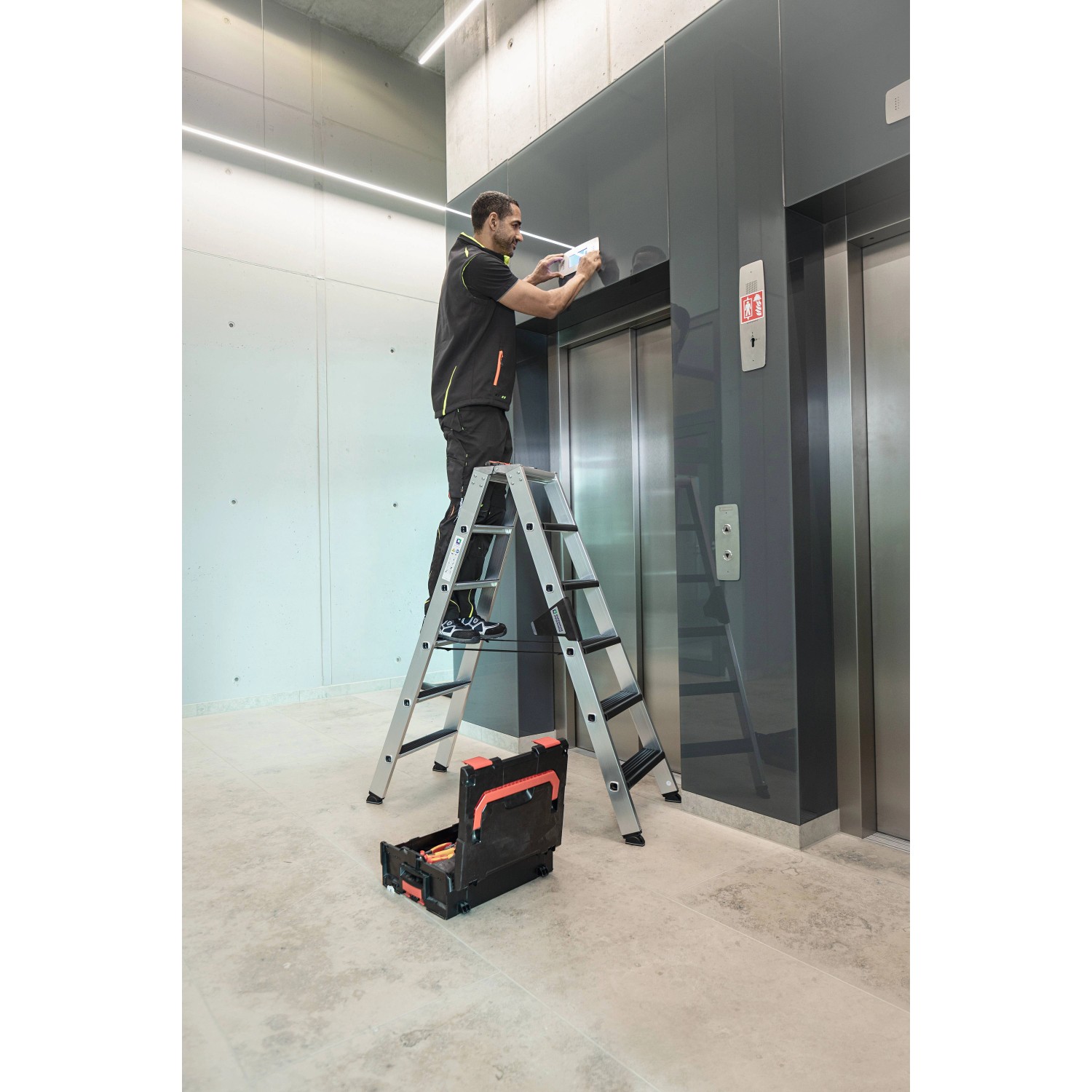 PROREGAL Stufen-Stehleiter mit Clip-Step Relax im Einsatz vor Aufzug. Aluminium Leiter, 2x7 Stufen.