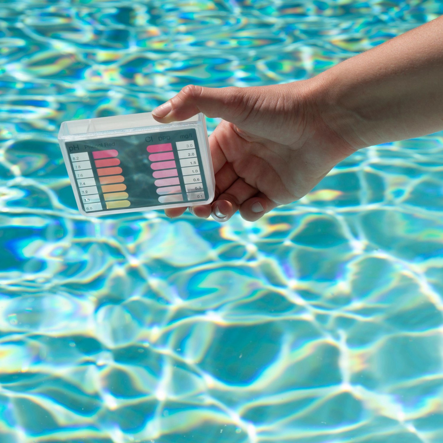 Bayrol Pooltester pH/Cl mit Farbskala zur Poolwasseranalyse in der Hand über Wasser.