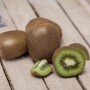 Mehrere Kiwis, ganze und angeschnitten, auf hellem Holzgrund. GROW by OBI Kiwi Jenny.