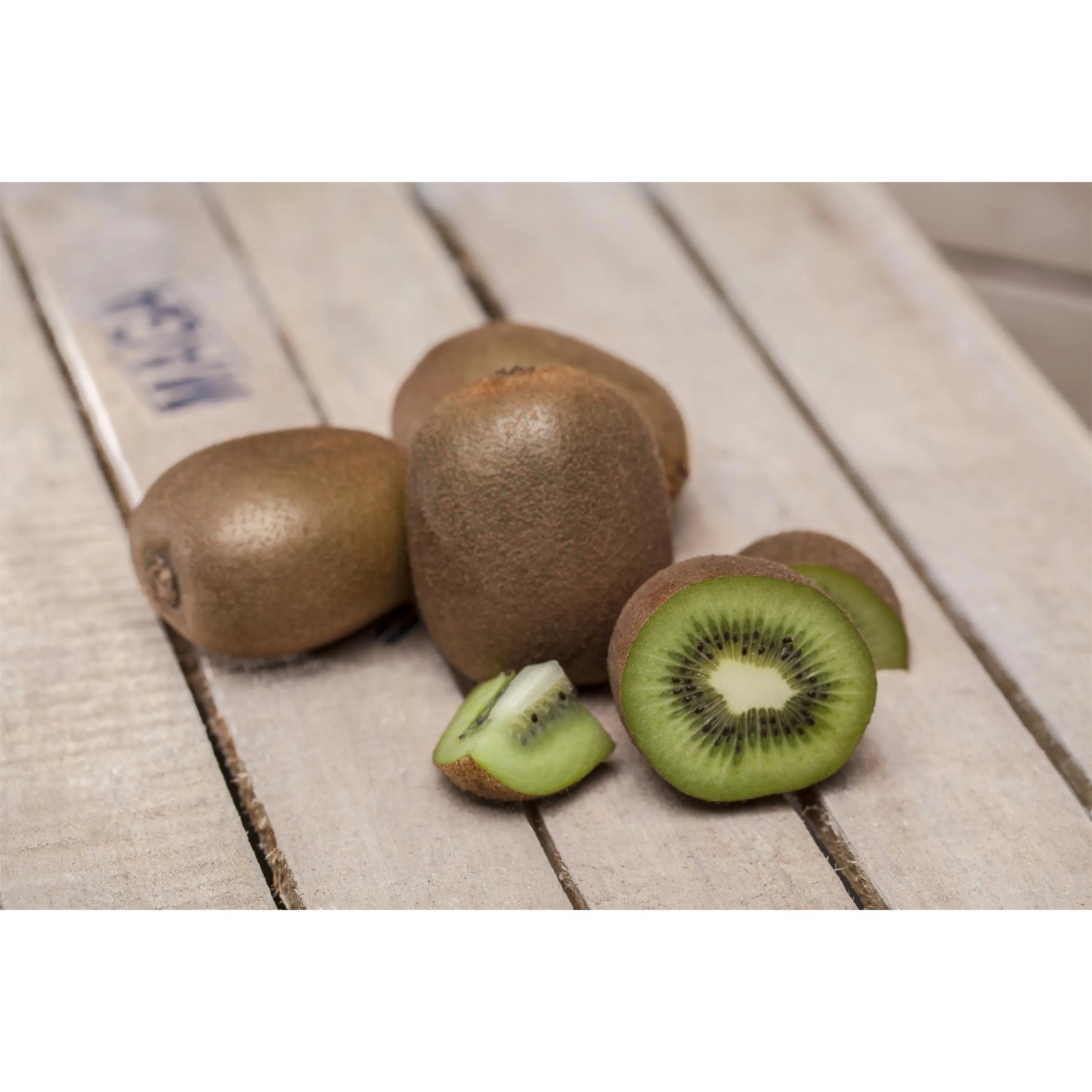 Mehrere Kiwis, ganze und angeschnitten, auf hellem Holzgrund. GROW by OBI Kiwi Jenny.