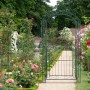 Dunkelgrüner Rosenbogen aus Eisen mit Tor als Rankhilfe im Garten. Ideal für Kletterpflanzen und als dekorativer Eingang.