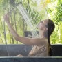Frau duscht hinter transparentem Duschrollo aus PVC/Aluminium. Wasserabweisender Spritzschutz für Dusche und Badewanne.