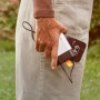 Fiskars Akku 12V 4Ah lädt Smartphone per USB-C. Weiße Powerbank in Hand, draußen.